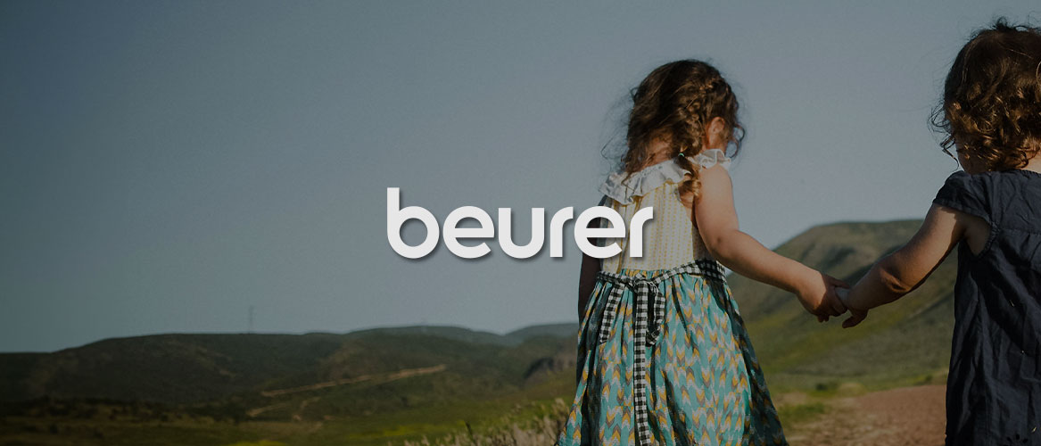 Zwei Kleine Mädchen laufen Hände haltend auf einem Feld. Mittig im Bild wird das beurer Logo dargestellt.